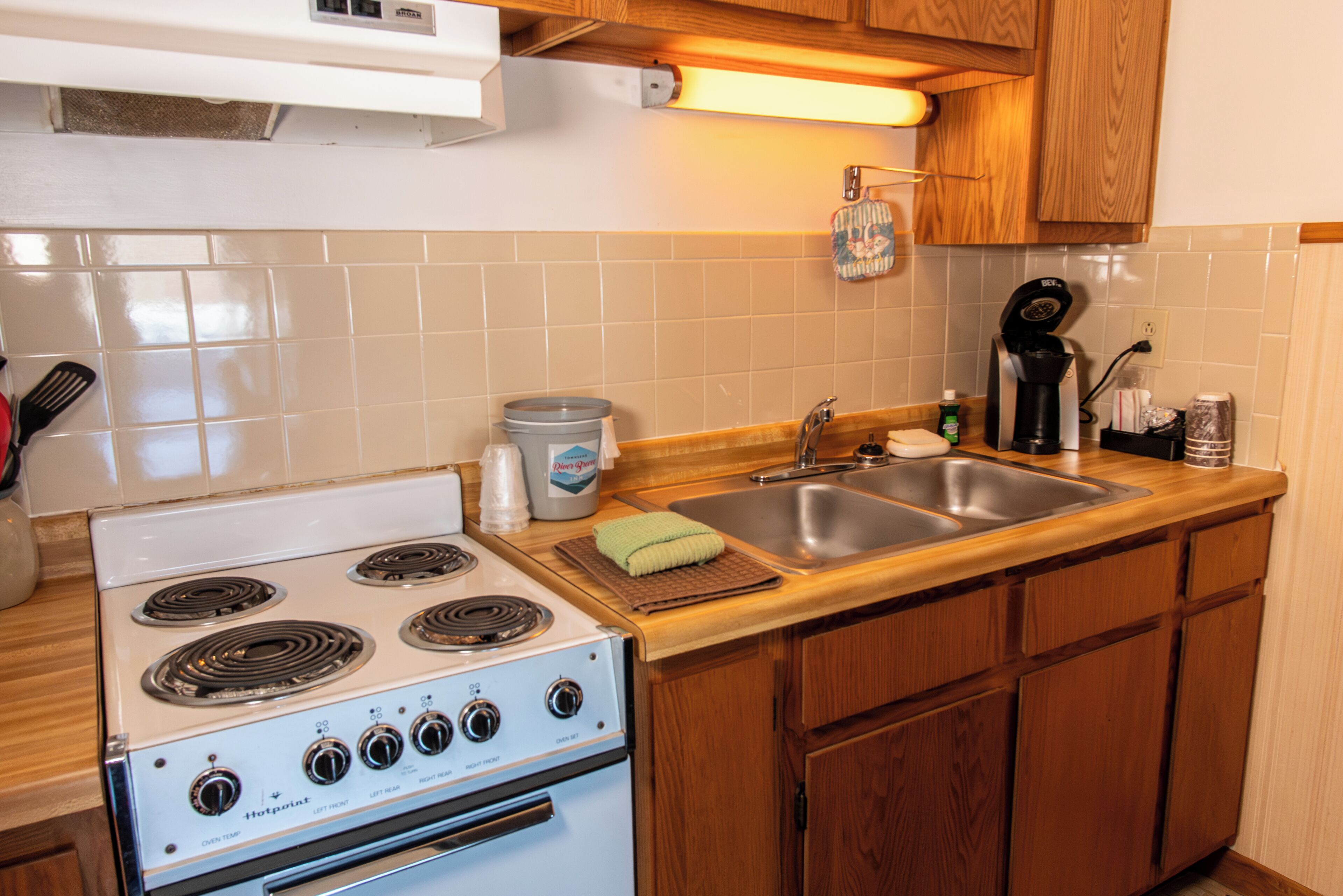 A kitchen with a white stove, a sink, wooden cabinets, and a backsplash.