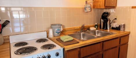 A kitchen with a white stove, a sink, wooden cabinets, and a backsplash.