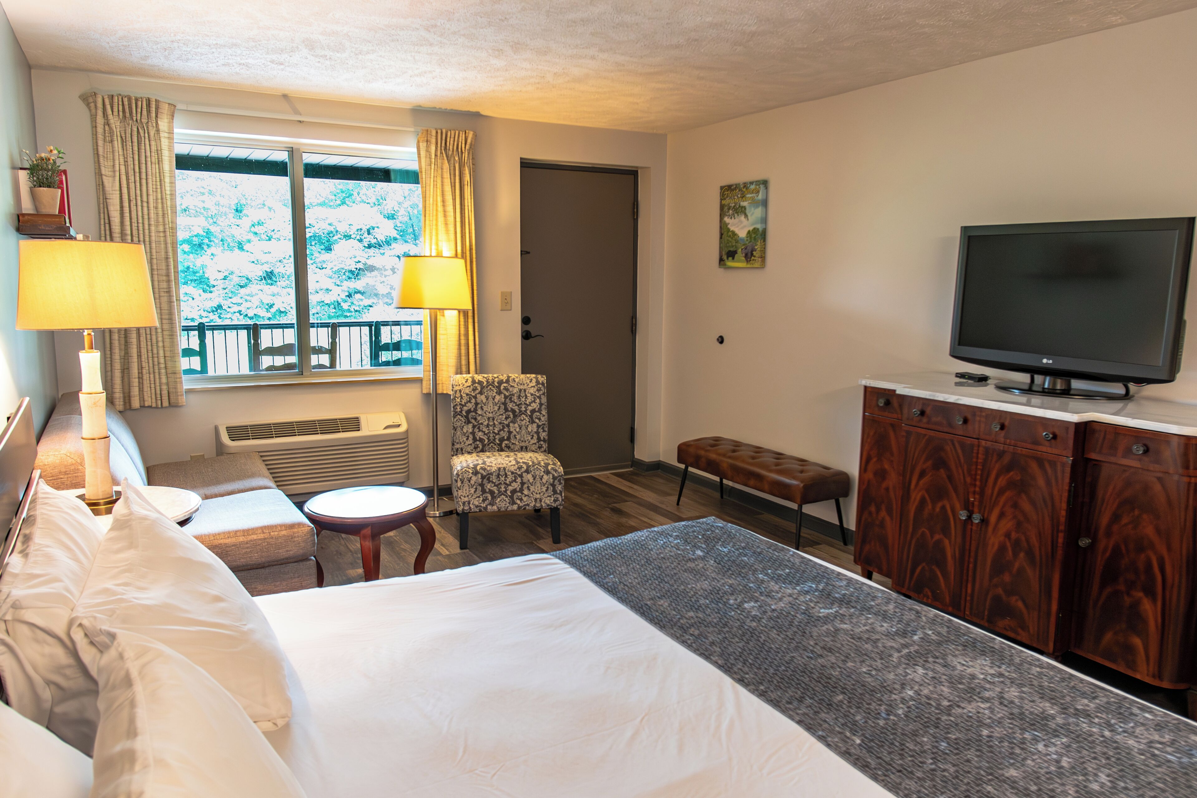 A hotel room with a bed, a desk, a chair, a TV, and a window with curtains.
