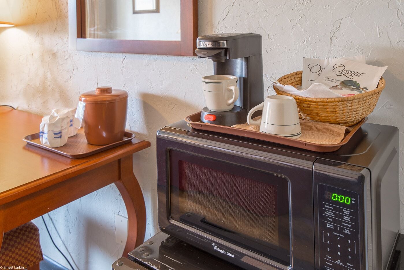 A microwave with a coffee maker and a basket of bread on top.