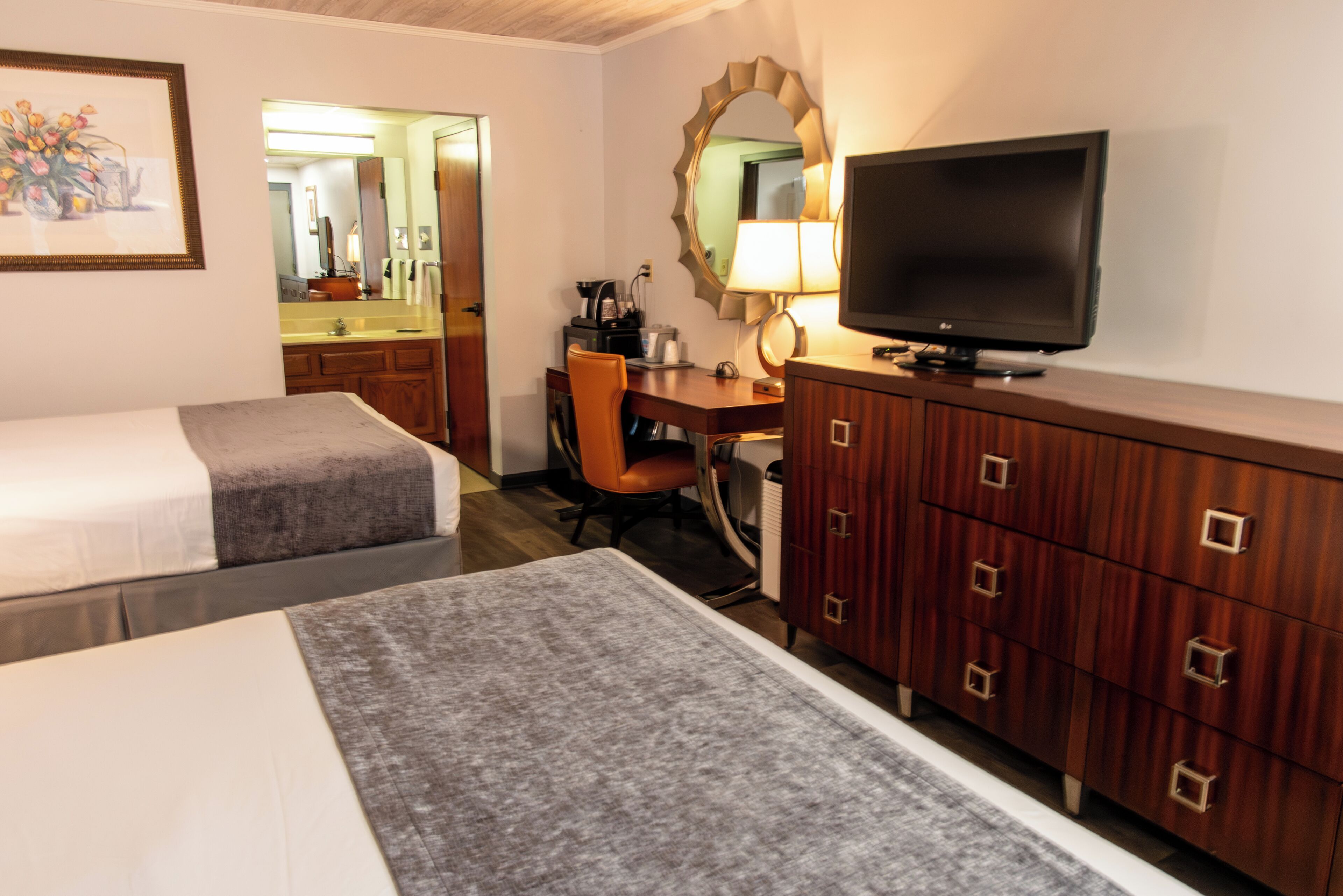 A hotel room with two beds, a desk with a chair, a television, and a dresser.