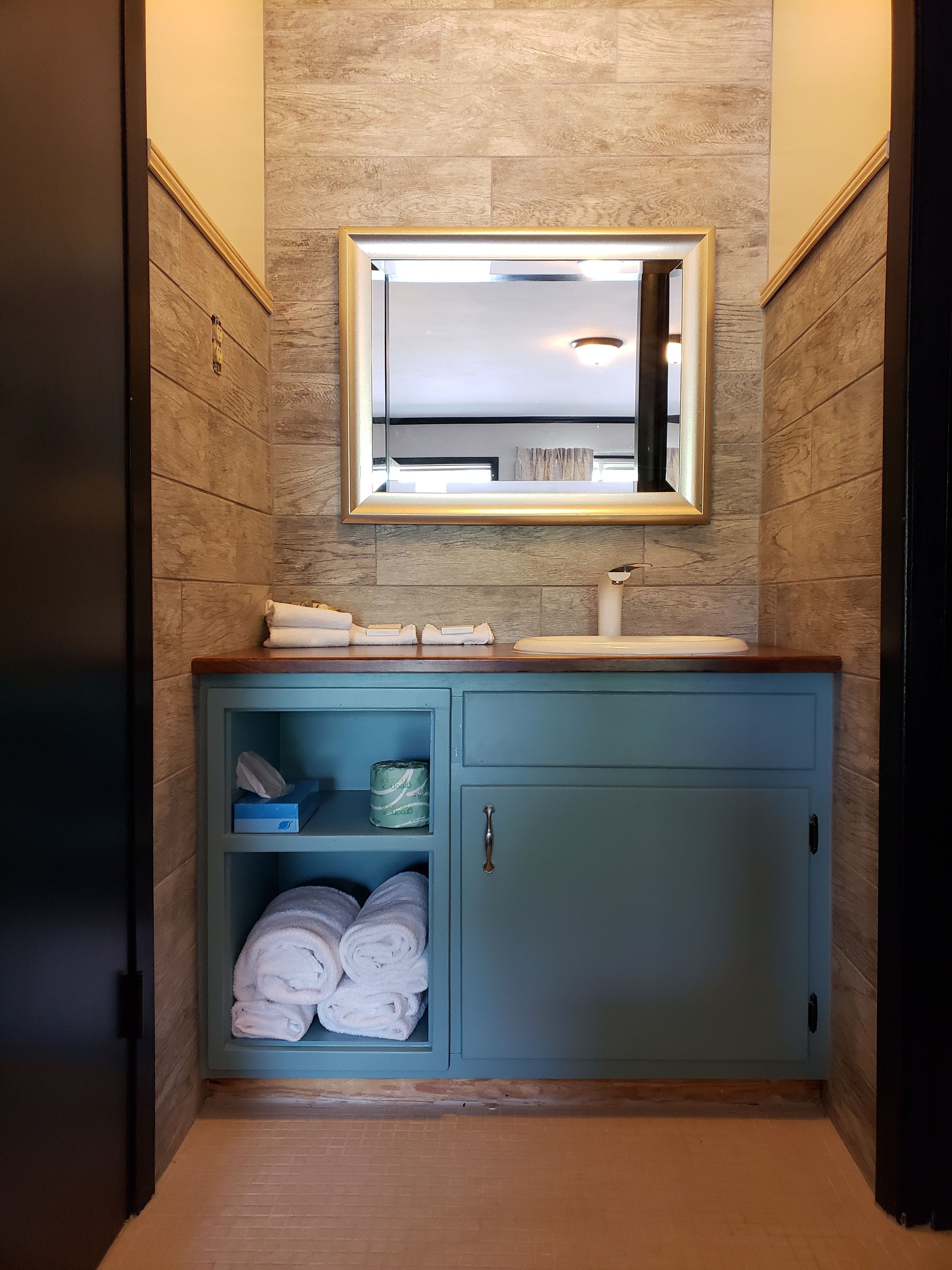 A bathroom with a wooden wall, a blue cabinet with towels, and a mirror above the sink.