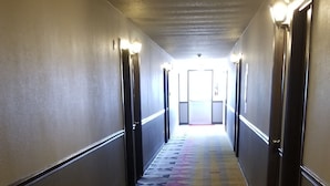 A hotel hallway with patterned carpet, doors on both sides, and overhead lighting. - Alexander House Motel (Park River)