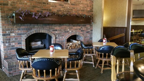 A restaurant with brick walls, a fireplace, wooden tables, and black upholstered chairs. - Alexander House Motel (Park River)