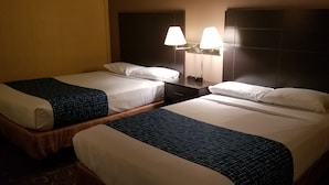 Two adjacent hotel beds with white linens and dark blue blankets, a nightstand with a lamp, and a dark headboard. - Alexander House Motel (Park River)