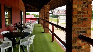 A motel with outdoor seating, a brick wall, and a view of the parking lot. - Alexander House Motel (Park River)