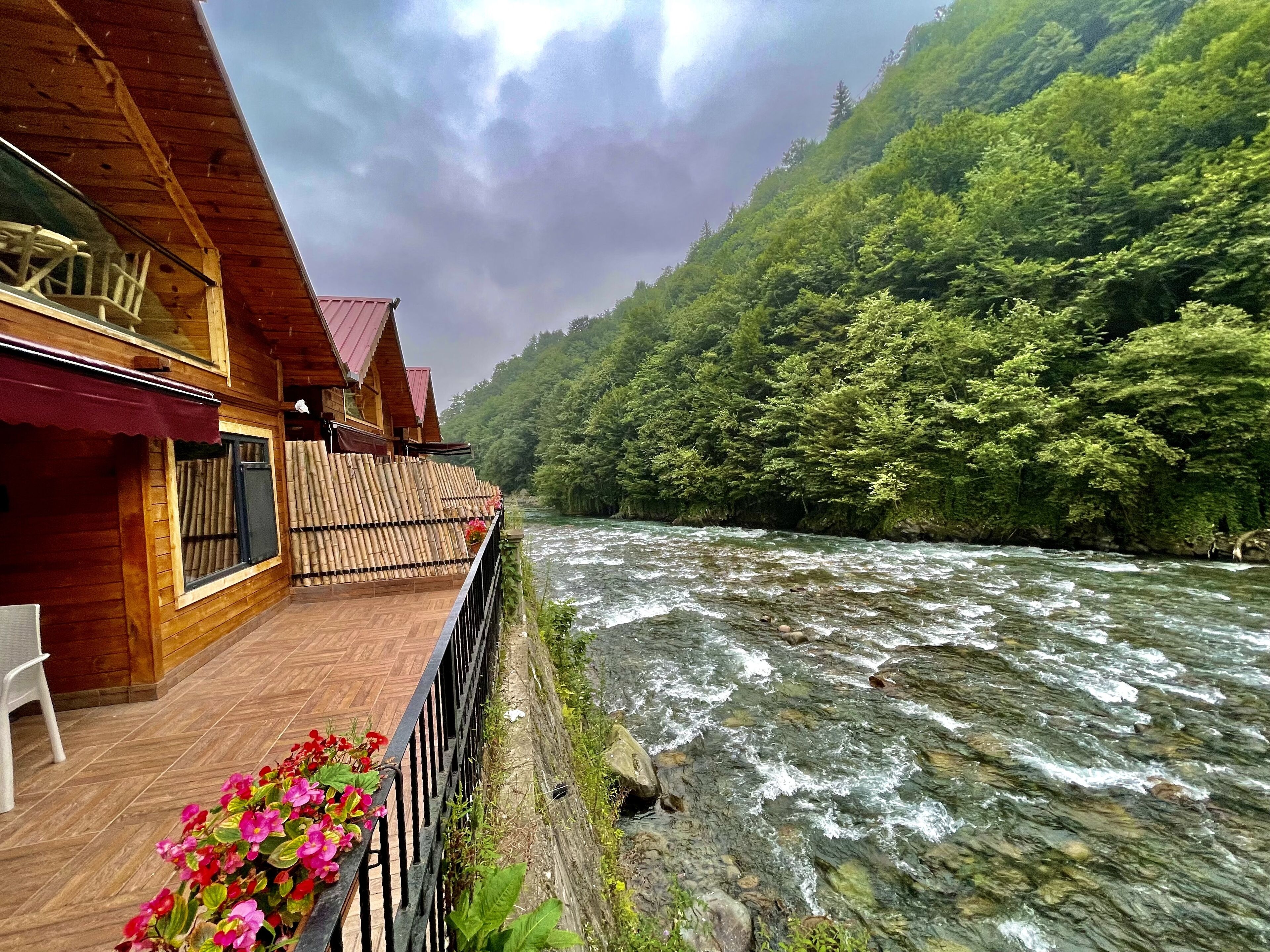 Een houten hut met een balkon dat uitkijkt over een rivier, omgeven door dicht bos.