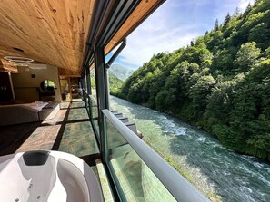 Una stanza con parete di vetro che si affaccia su un fiume, soffitto in legno e un'area salotto con divano e tavolino.