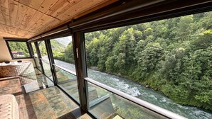 Una habitación con amplios ventanales que dan a un río y un bosque.