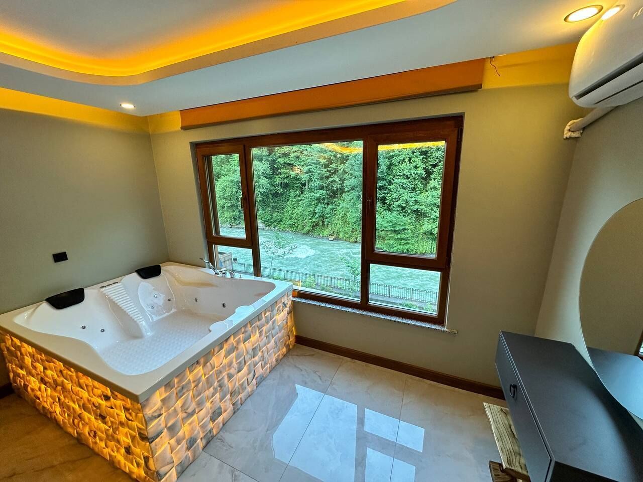 Un baño moderno con una bañera grande, un televisor y vistas a un río.
