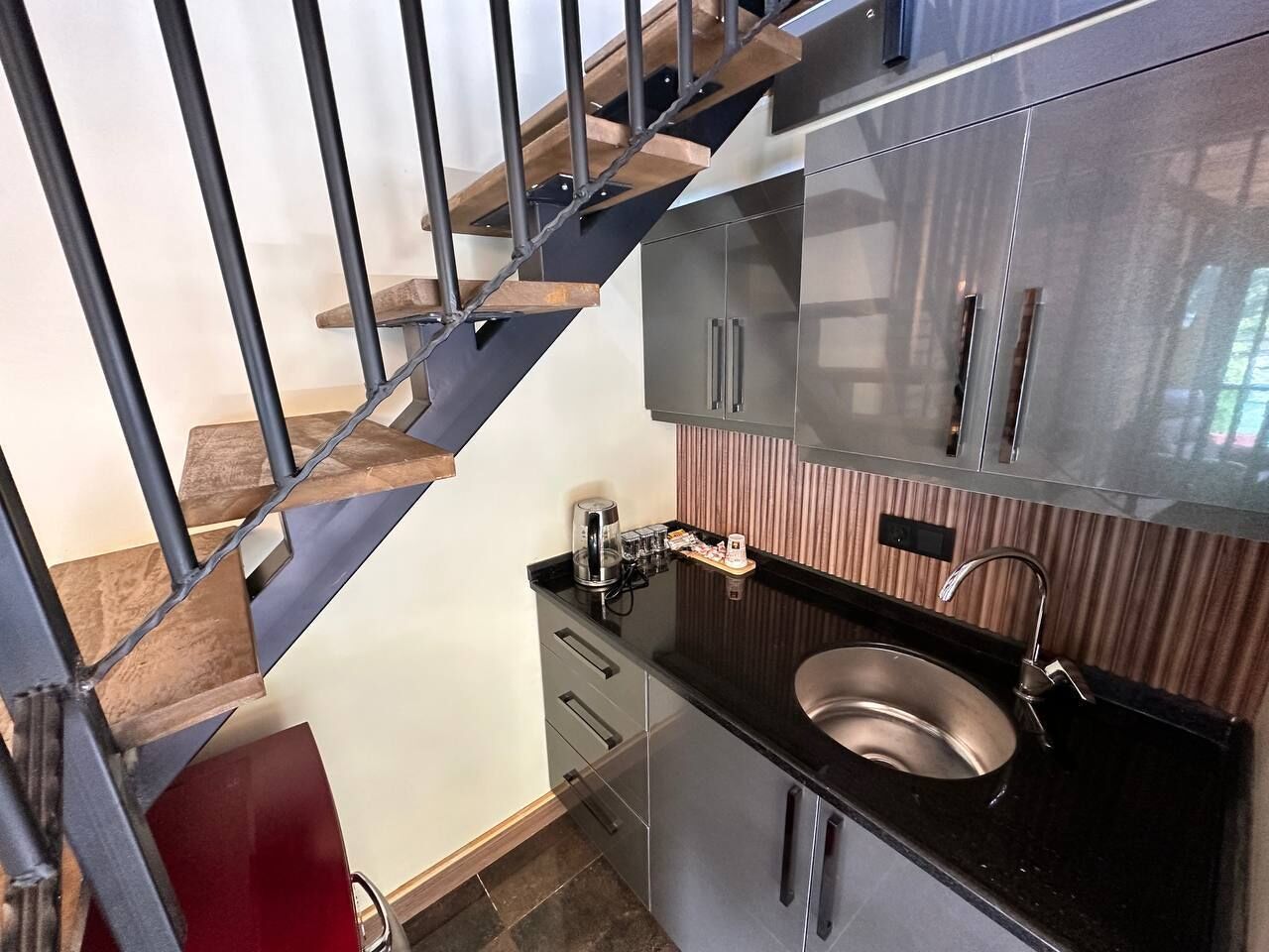 Une cuisine moderne dotée d’un évier en acier inoxydable, d’un escalier en bois et d’une machine à café.