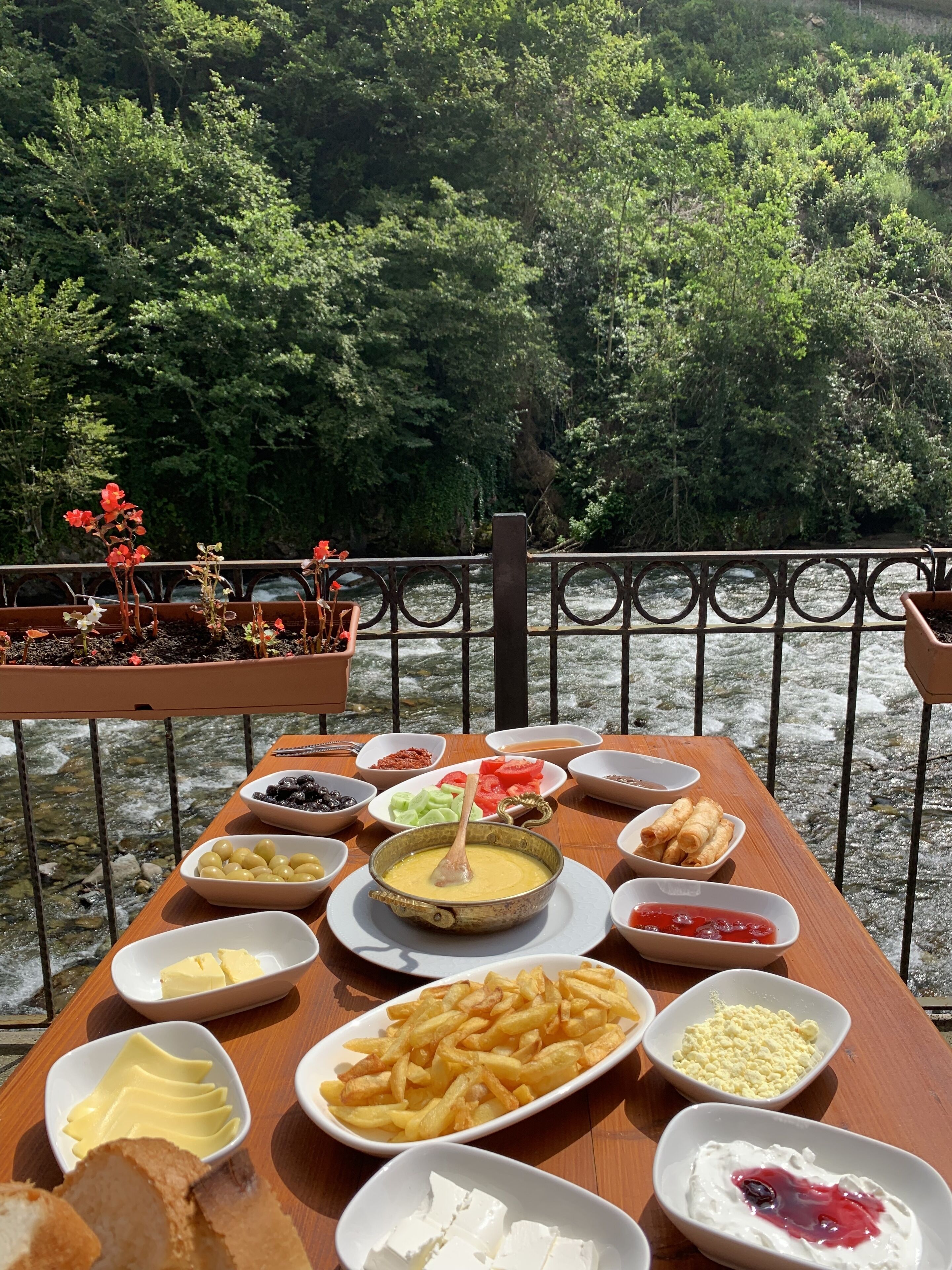 A table set with various food items and a view of a river and forest.
