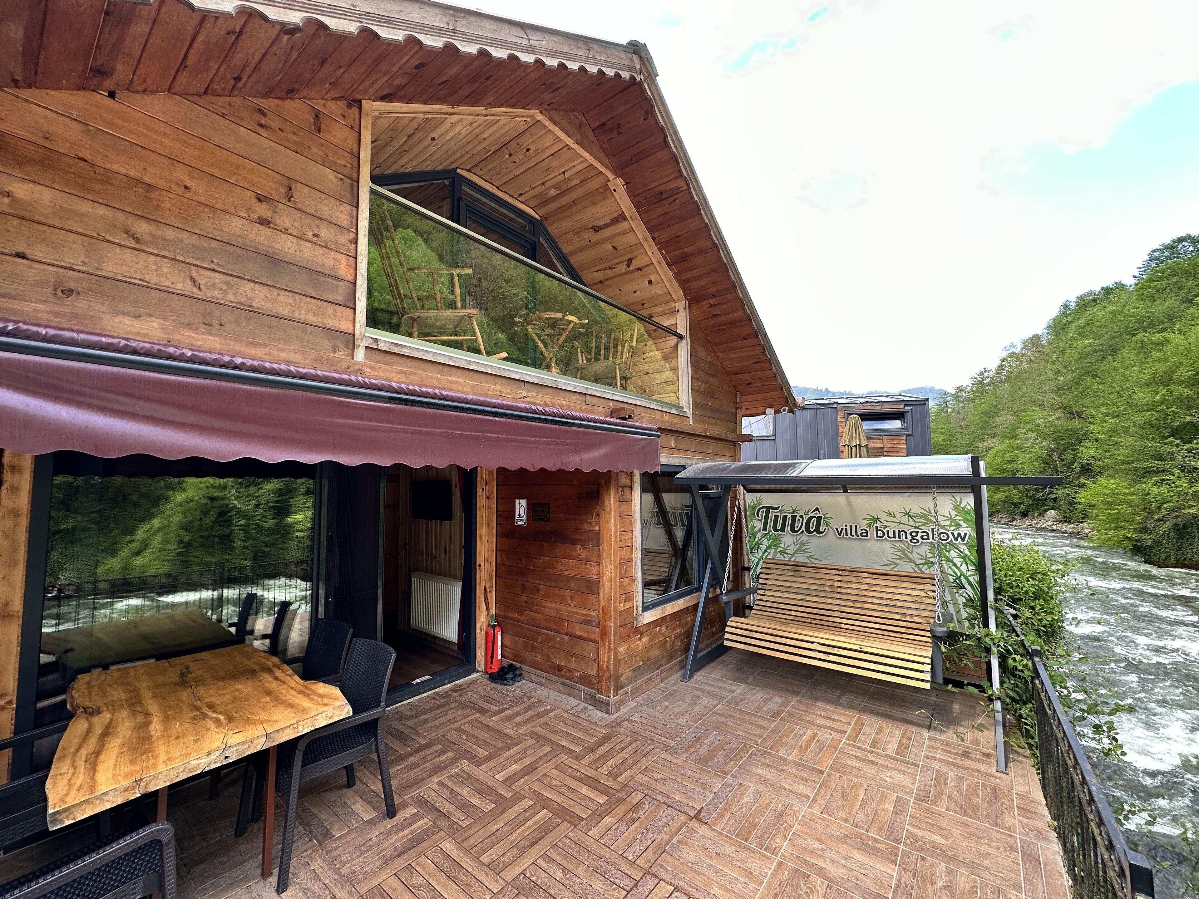 Una cabaña de madera con comedor y vista al río.