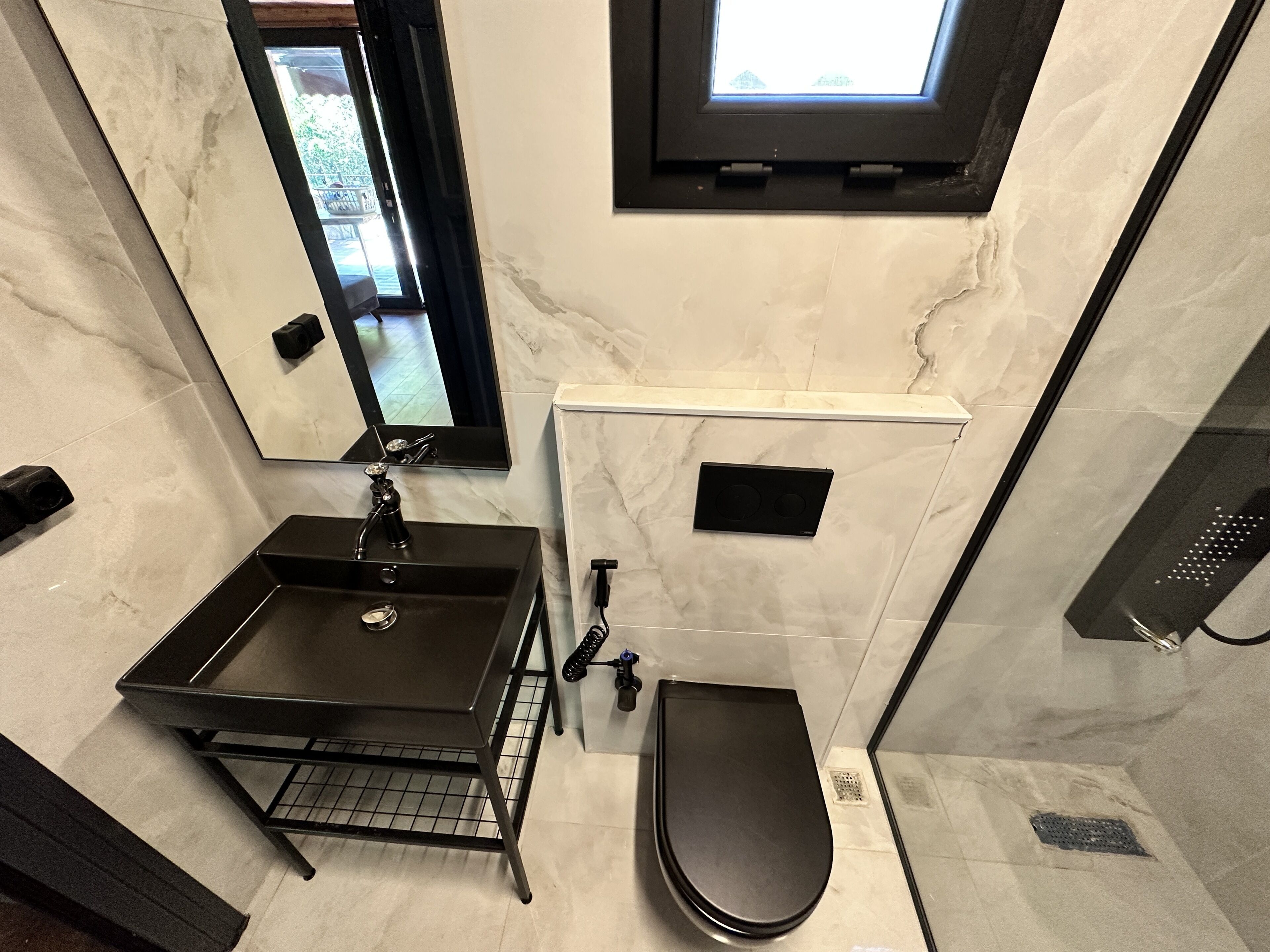 Un baño con lavamanos negro, un espejo, una ventana, inodoro y zona de ducha.