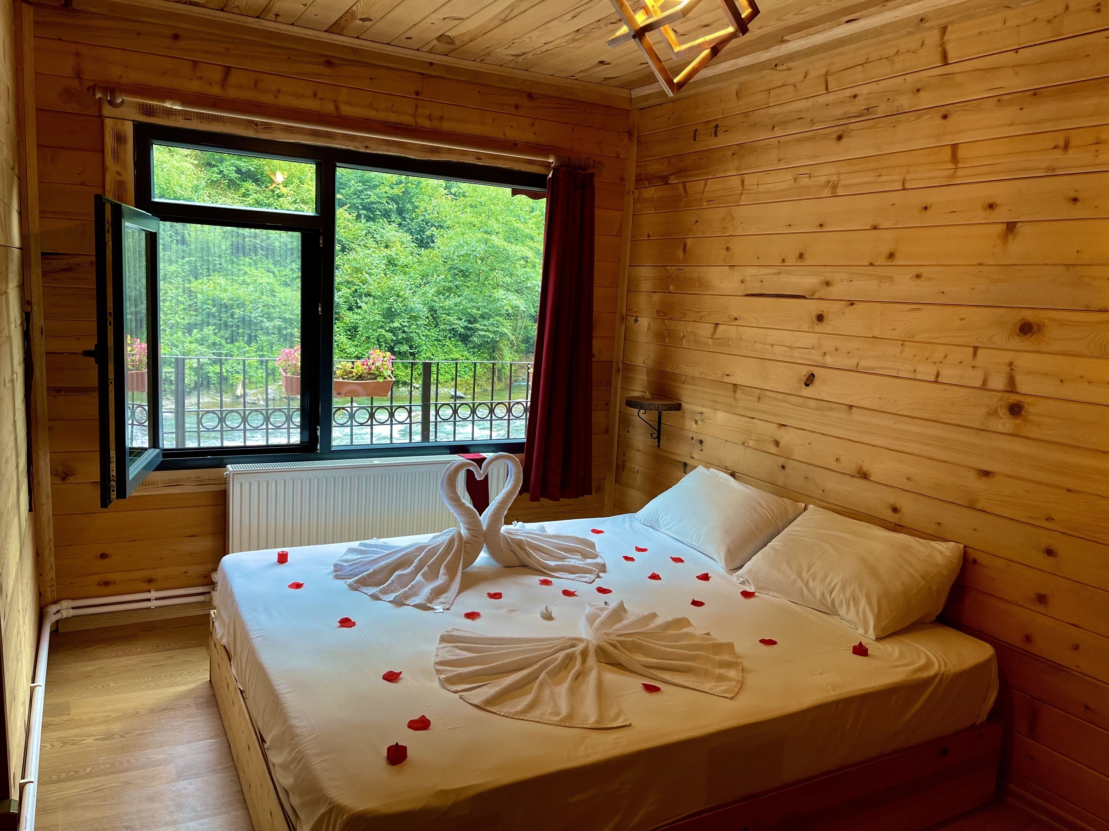 A wooden cabin room with a bed, a window, and a view of greenery outside.