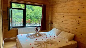 A wooden cabin room with a bed, a window, and a view of greenery outside.