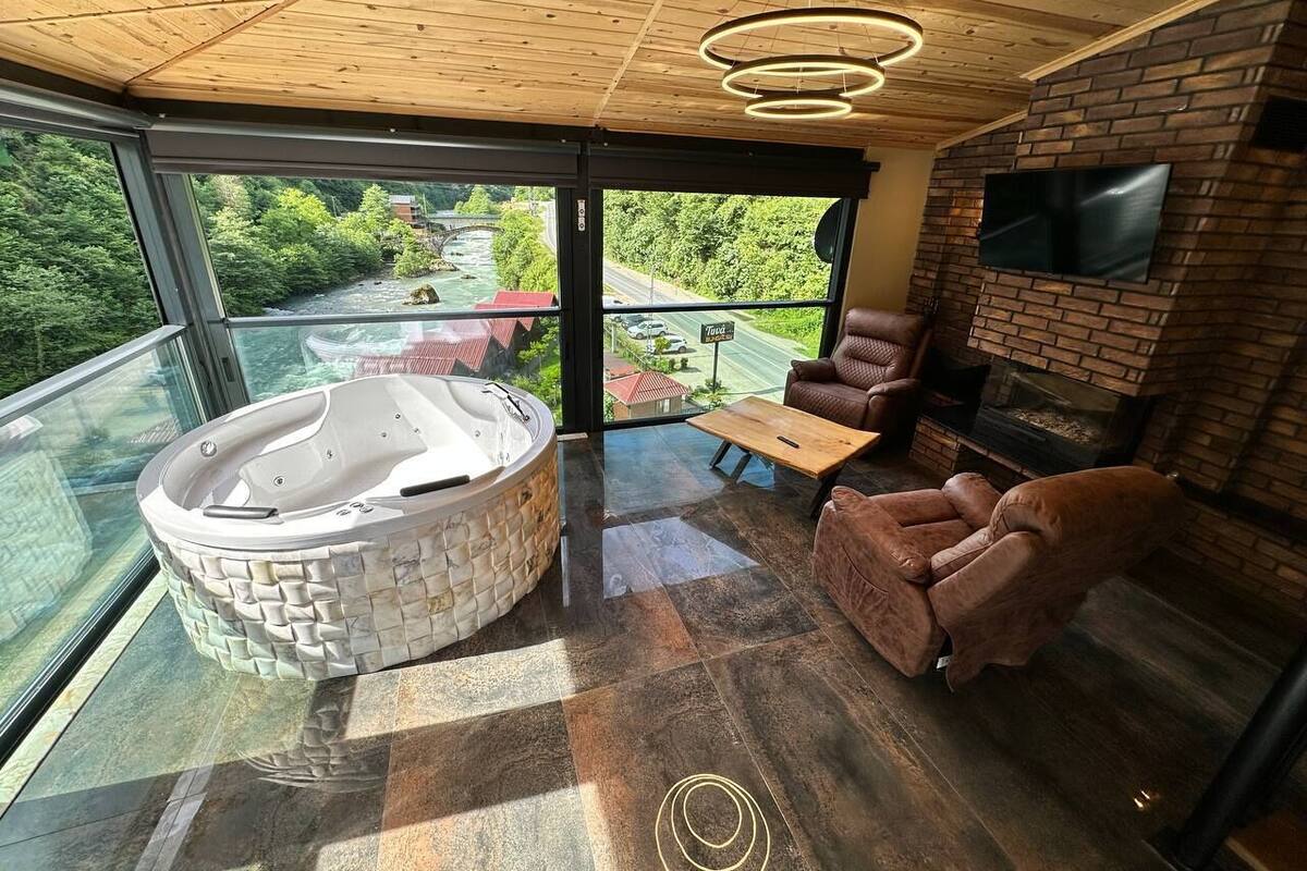 Une chambre moderne avec un mur de verre, un jacuzzi, une cheminée et des fauteuils en cuir.