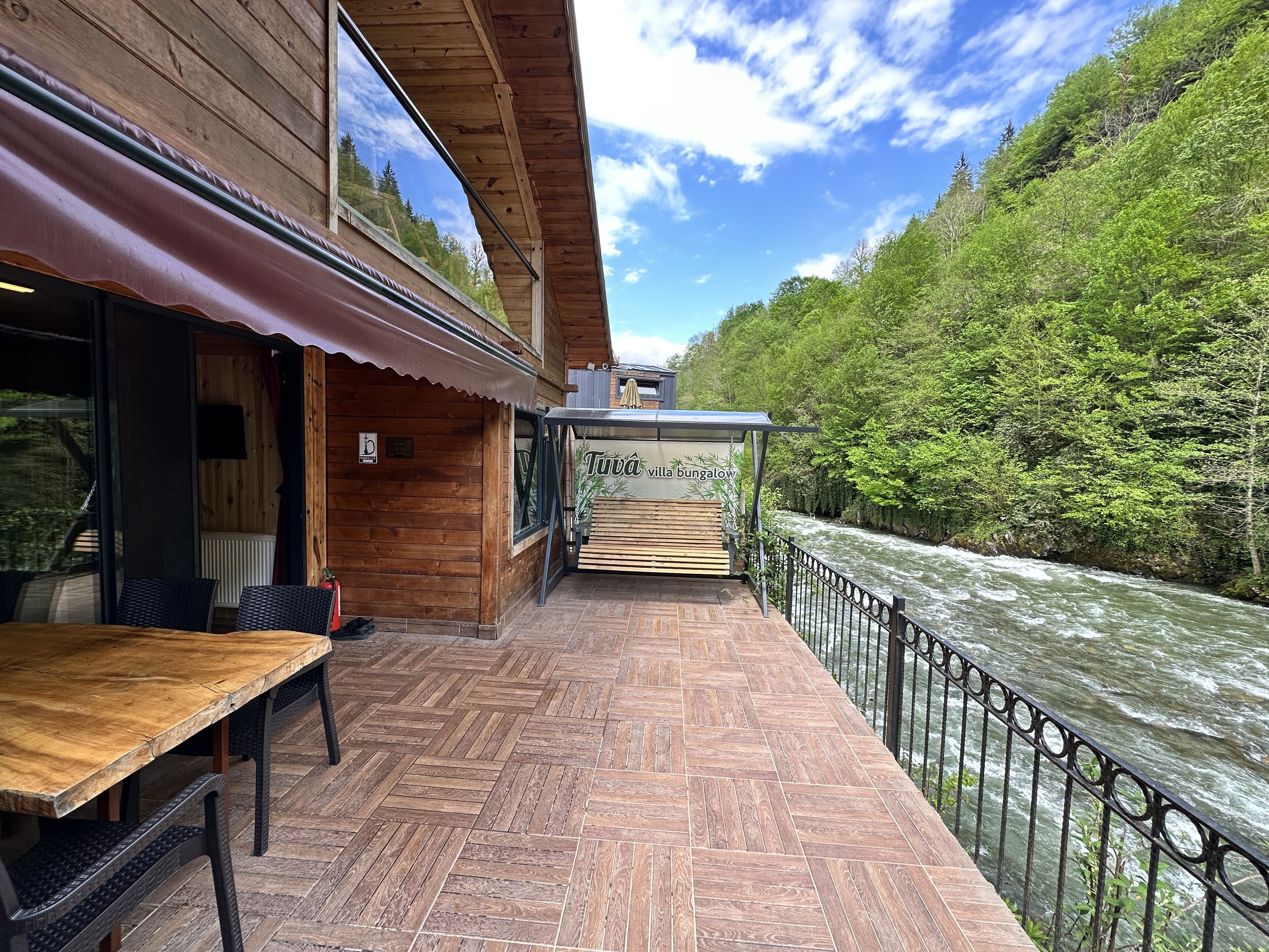 A wooden bungalows with a river view, outdoor seating, and a sign reading "Tuva villa bungalow".