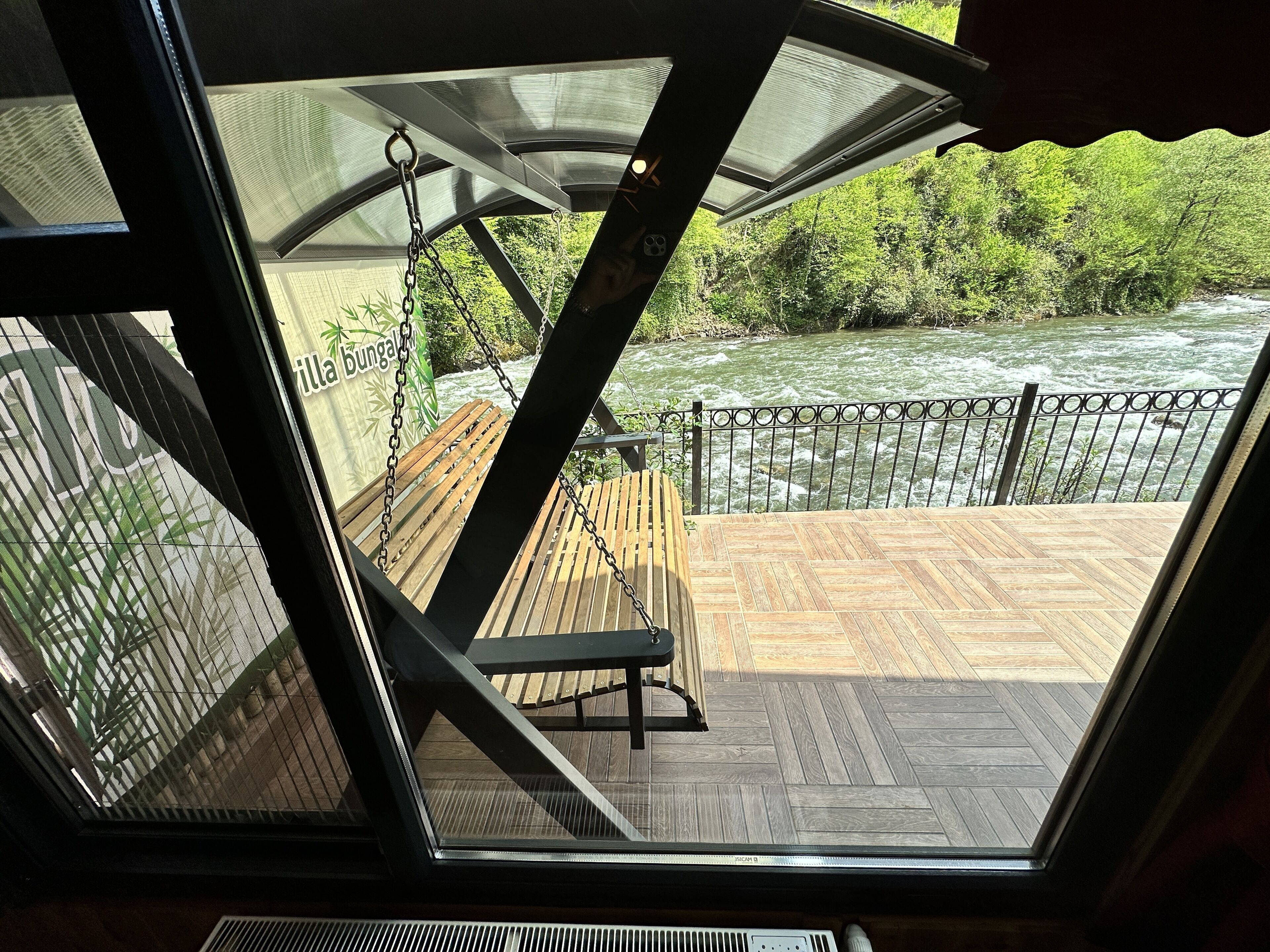 A view from a room with a large window overlooking a wooden deck and a river.