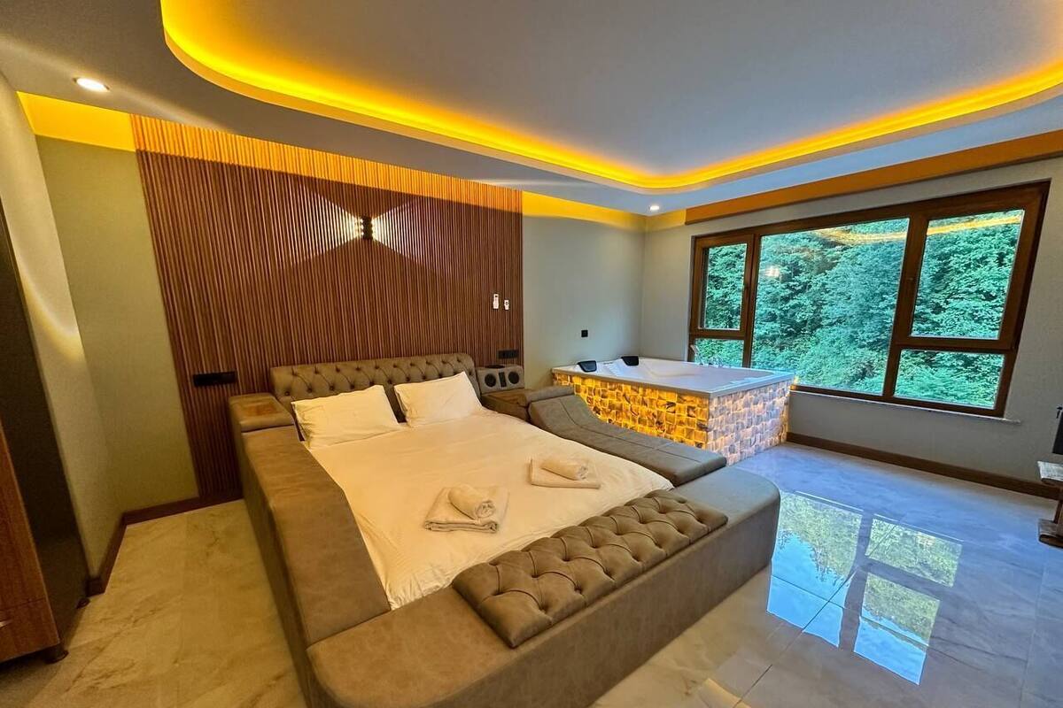 Une chambre spacieuse avec un grand lit, un coin salon et une vue sur la verdure environnante.