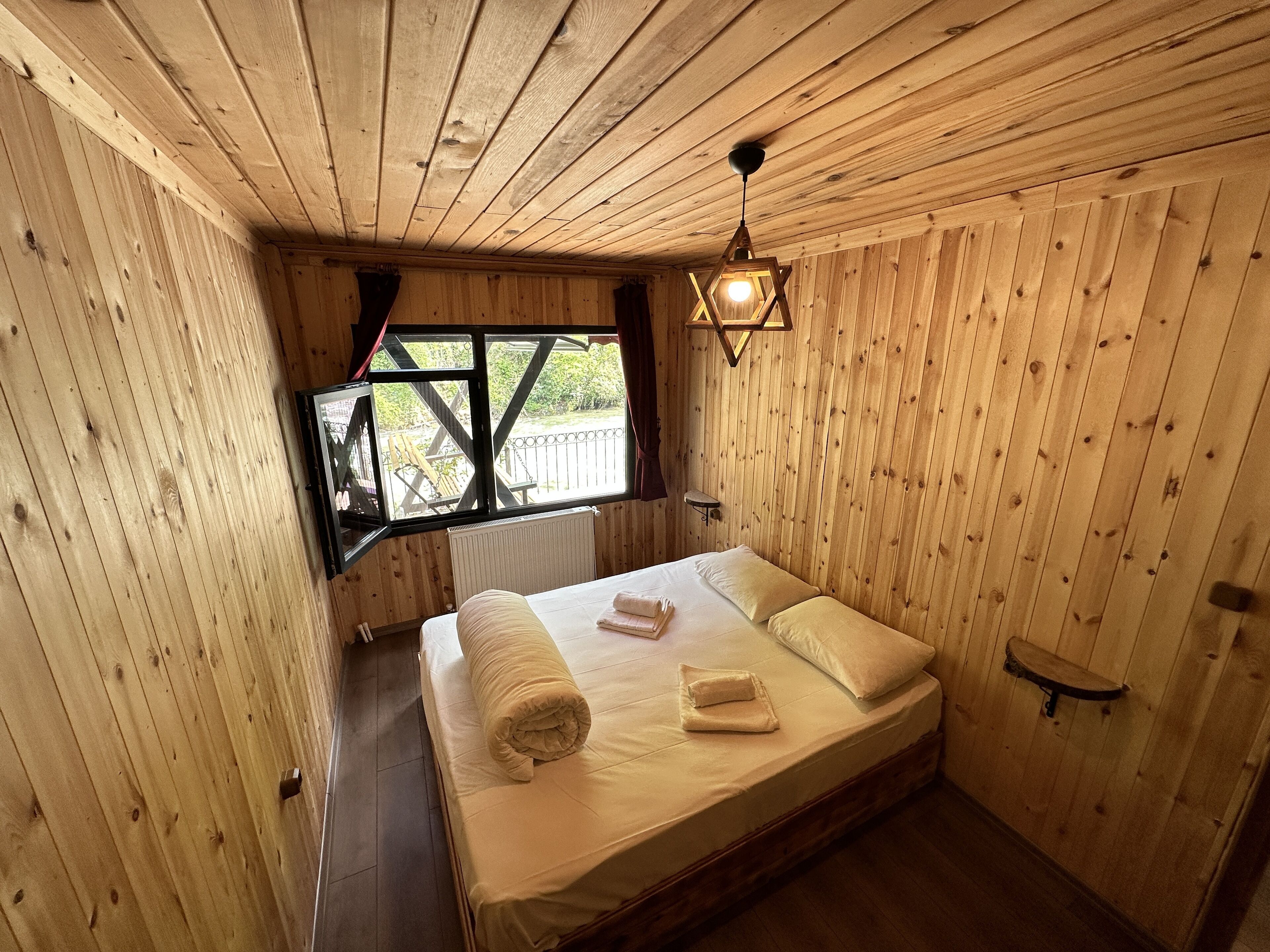 Quarto com painéis de madeira, uma cama, uma janela e um lustre.