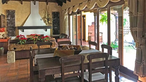 A spacious dining area with a high ceiling, a fireplace, and a view of the outdoor patio. - Casa El Descansar (Antigua Guatemala)