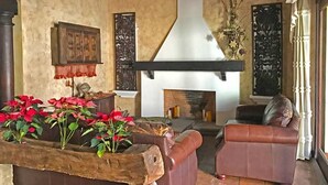 A cozy living room with a fireplace, leather sofas, and a wooden planter with red flowers. - Casa El Descansar (Antigua Guatemala)