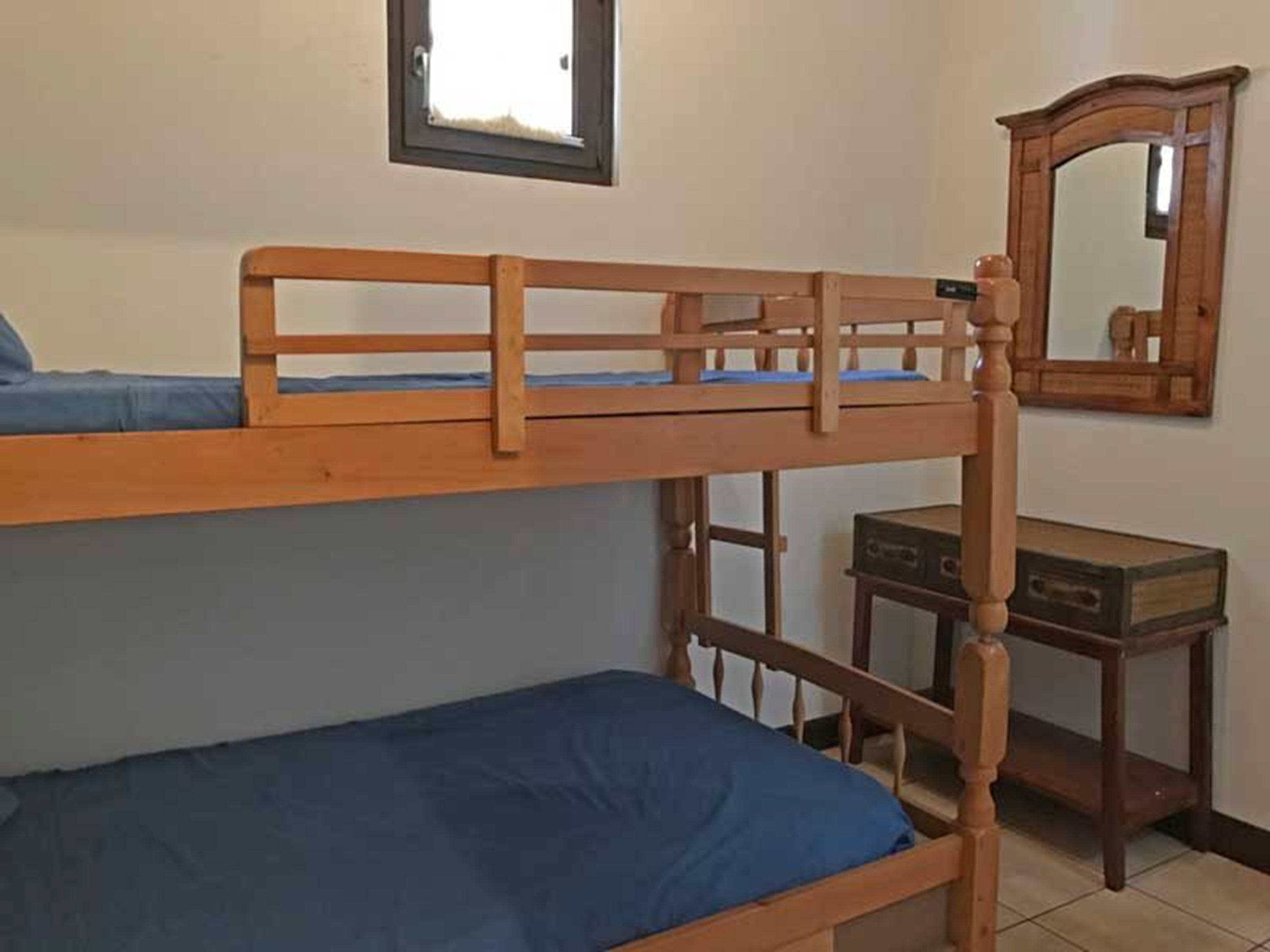 Habitación con literas, un cabecero de madera, una mesita pequeña y un espejo en la pared.