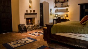 A cozy bedroom with a fireplace, a bed with a green blanket, and a quilt on the floor. - Casa Las Ruinas (Antigua Guatemala)