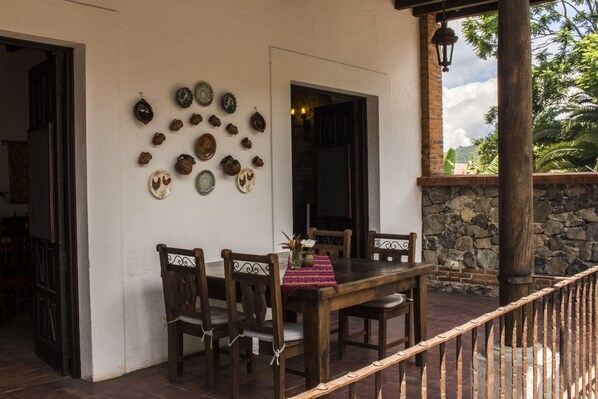 Un comedor con una mesa y sillas de madera, una pared decorativa con varios platos y una pared de piedra con barandilla de madera.