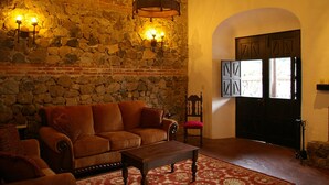 A stone-walled room with a wooden door, a brown sofa, and a red chair. - Casa Las Ruinas (Antigua Guatemala)