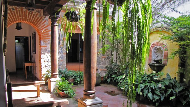 A courtyard with stone columns, hanging plants, and a fountain. - Casa Real (Antigua Guatemala)