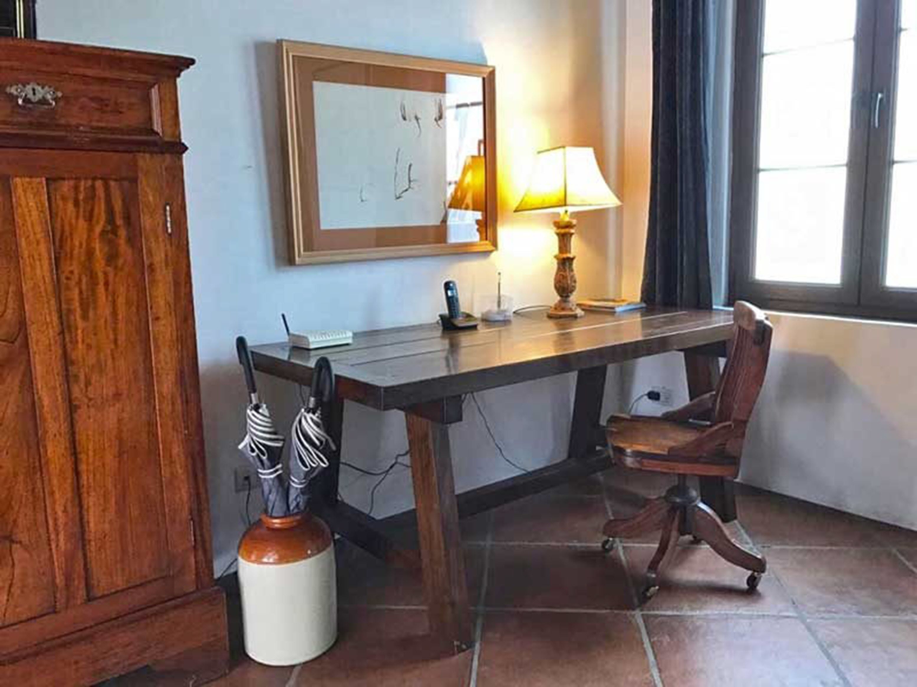A room with a wooden desk, a chair, a lamp, a framed picture on the wall, and a cabinet.