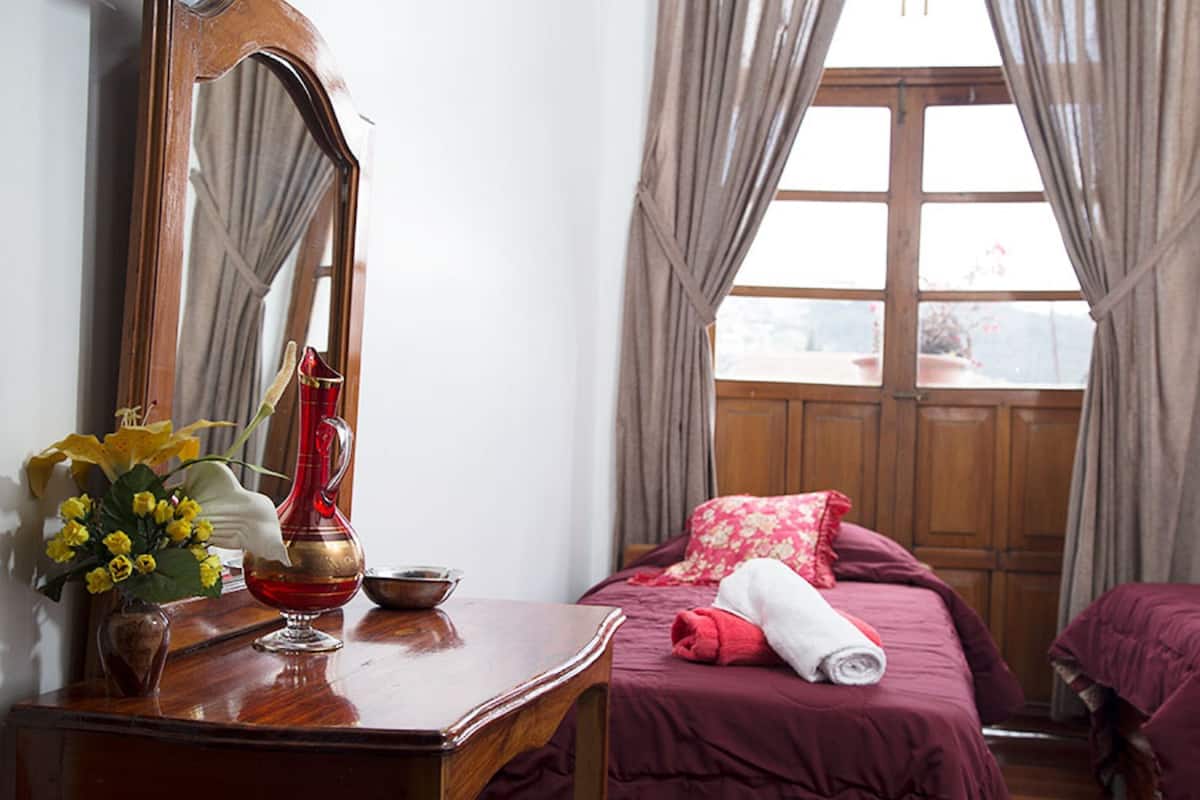 A hotel room with a wooden dresser, a mirror, a vase with yellow flowers, a red vase, and a bed with a red blanket and pillows.