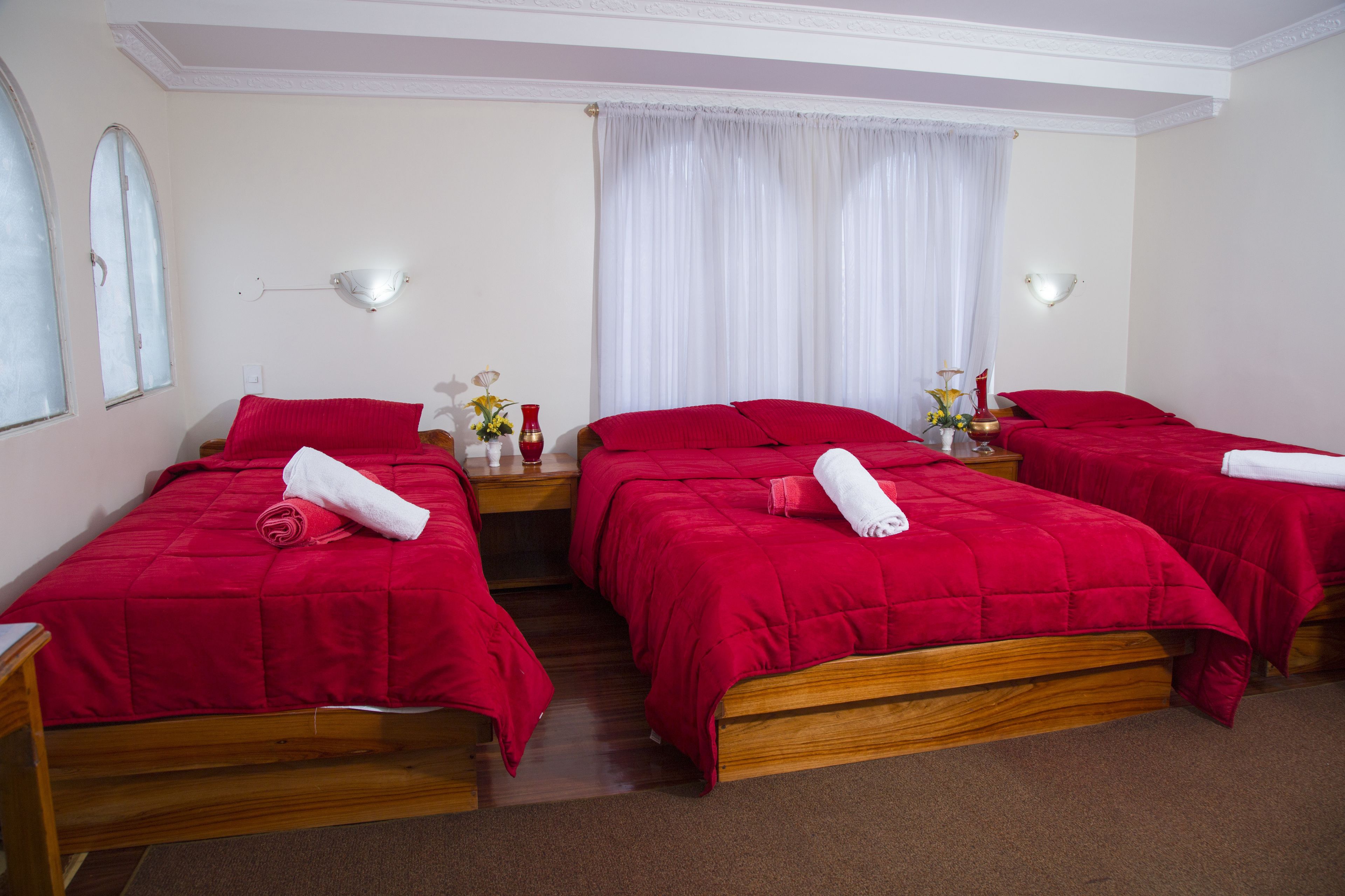 A hotel room with three wooden beds, each with red bedding and white towels.