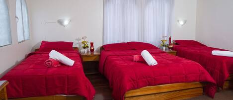 A hotel room with three wooden beds, each with red bedding and white towels.