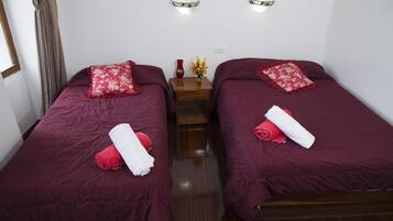A hotel room with two single beds, each with a red bedspread and matching pillows. There is a wooden nightstand between the beds with a vase of flowers and a red candle.