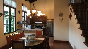 A kitchen with a dining area, featuring a large island, wooden cabinets, a stainless steel refrigerator, and a chandelier. - Casa Del Calvario (Antigua Guatemala)