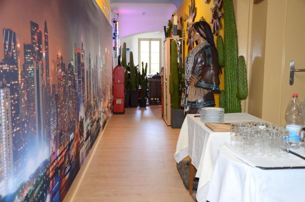 A hotel corridor with a cityscape mural, a cactus wall, and a table with glasses and bottles.
