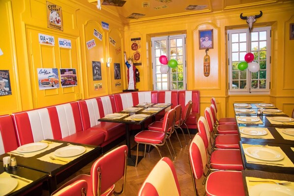 A diner with red and white striped booths, tables set with plates and cutlery, and a yellow wall adorned with various posters and signs.