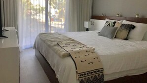 Ein Hotelzimmer mit einem großen Bett, einem Schreibtisch und Blick ins Freie durch transparente Vorhänge.