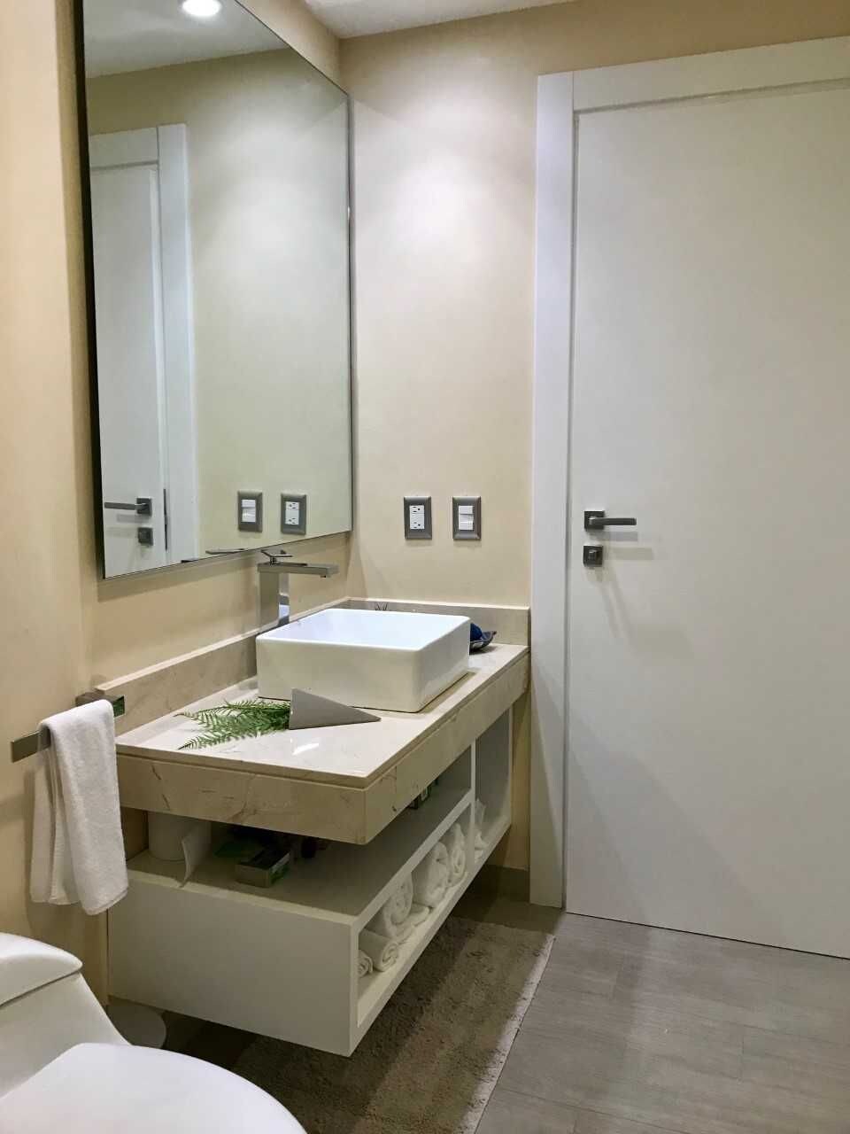 Een badkamer met een witte wastafel, spiegel en deur. Er zijn twee stopcontacten op de muur.