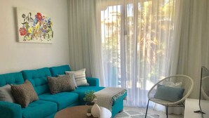 Ein Wohnzimmer mit einem türkisfarbenen Sofa, einem runden Couchtisch, einem weißen Sessel und einem Gemälde an der Wand.