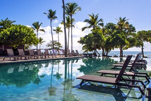 A pool area with lounge chairs and palm trees, overlooking a body of water. - Kûara Hotel (Porto Seguro)