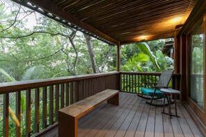 A wooden deck with a bench and a rocking chair, surrounded by lush greenery. - Kûara Hotel (Porto Seguro)