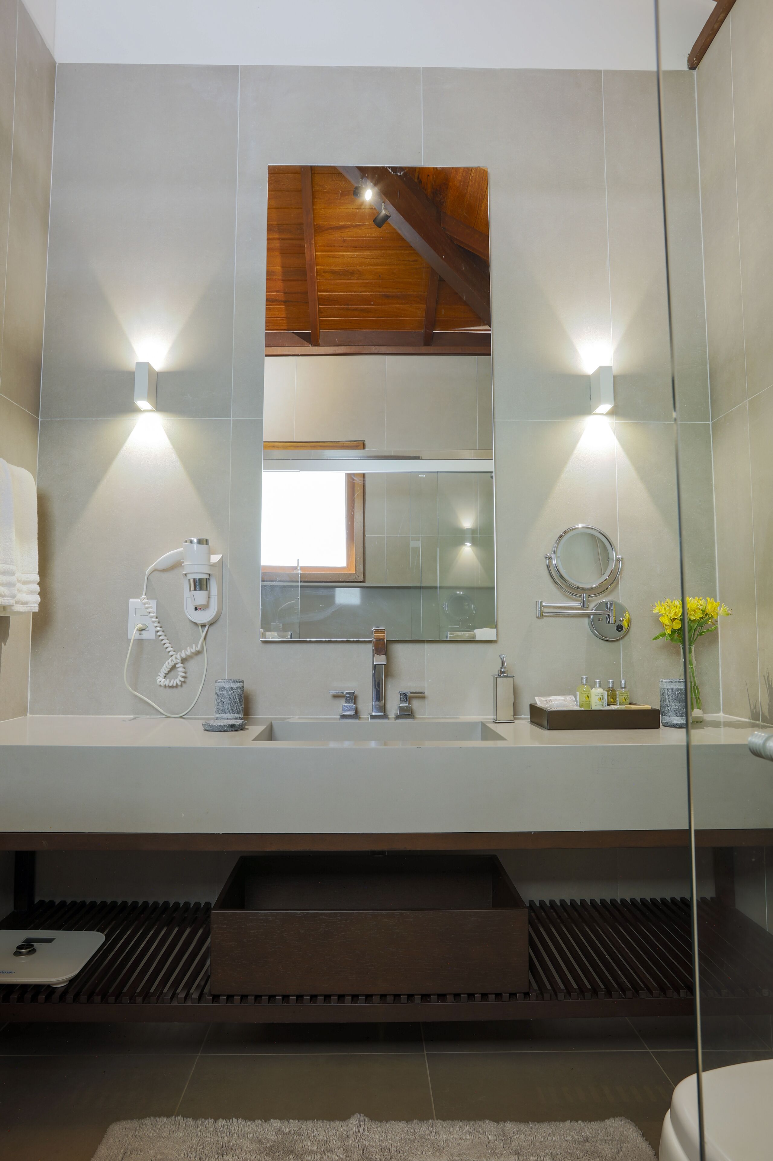 Un baño moderno con un espejo grande, un perchero para toallas, un lavabo y un mueble de tocador con artículos de aseo.