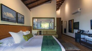A modern hotel room with a large bed, a sofa, a dining area, and artwork on the walls.