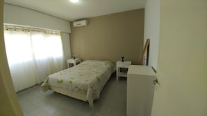 Un dormitorio con una cama, dos mesitas de noche, un escritorio, aire acondicionado y un espejo.