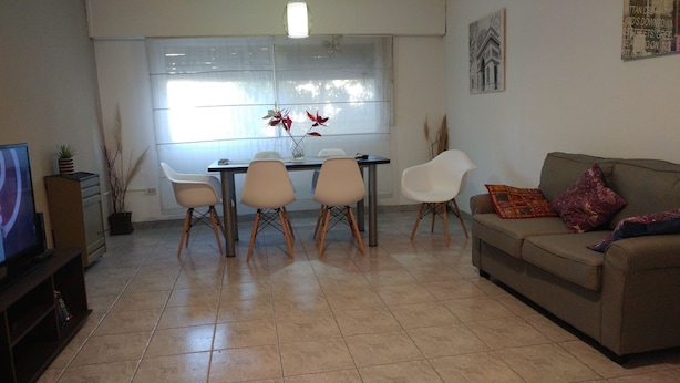 Una sala de estar con sofá, televisión, mesa de comedor y sillas.
