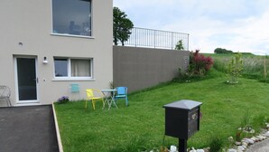 A modern building with a flat roof, a large window, and a door. There is a small garden with a mailbox, a yellow chair, and a blue chair. - Nice countryside studio near city (Formangueires)